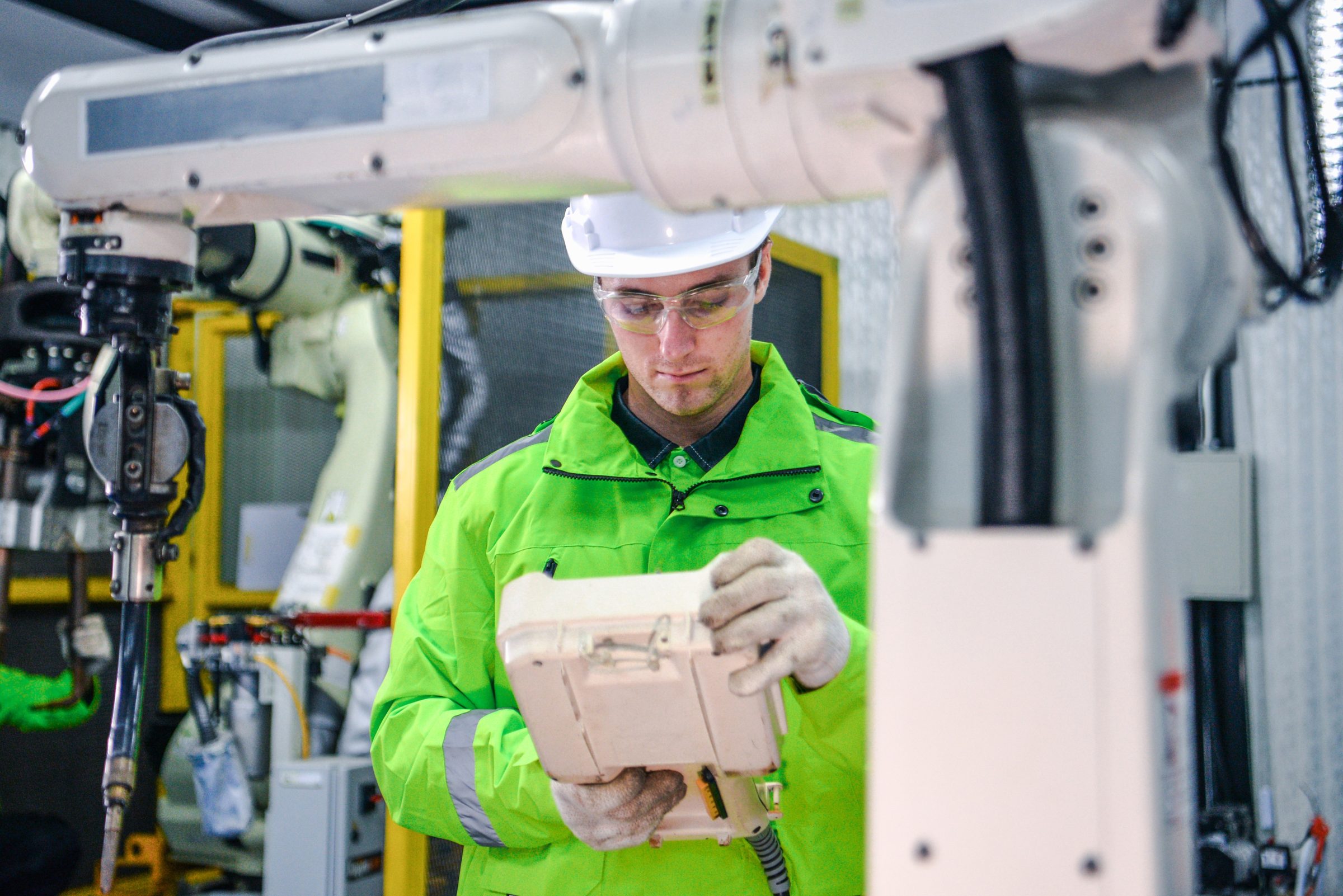 Engineer programming an industrial robot arm with a teach pendant